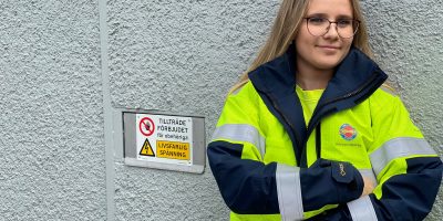 Tjej framför står lutad mot en stenvägg med skylt 